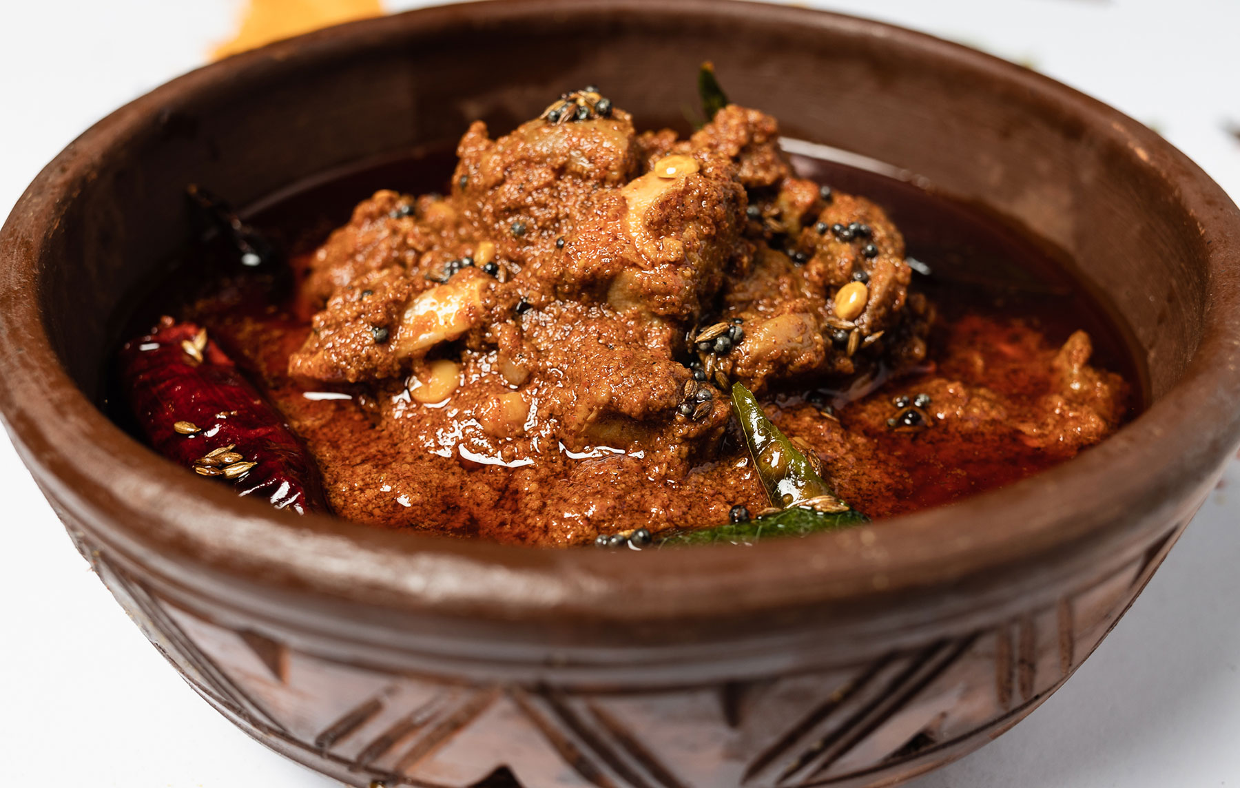 Close-up of spicy mutton pickle served in a traditional clay bowl, garnished with whole red chillies and mustard seeds