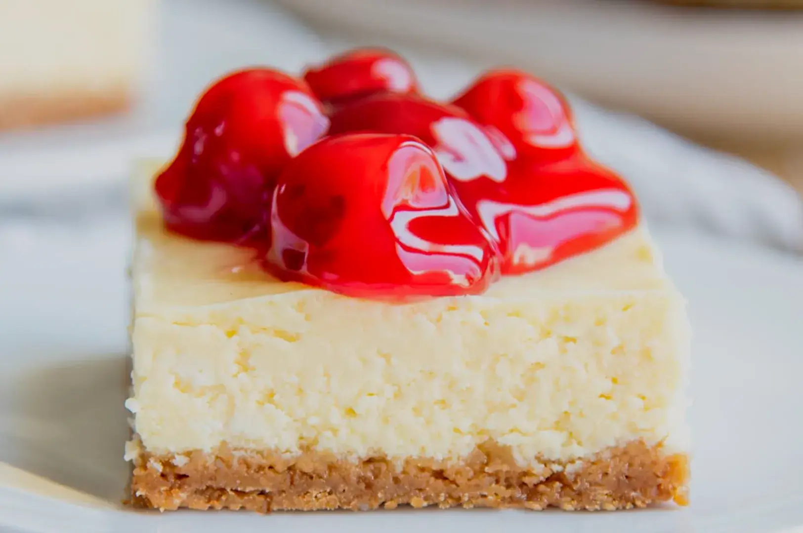 A slice of cheesecake topped with glossy red cherries on a white plate.