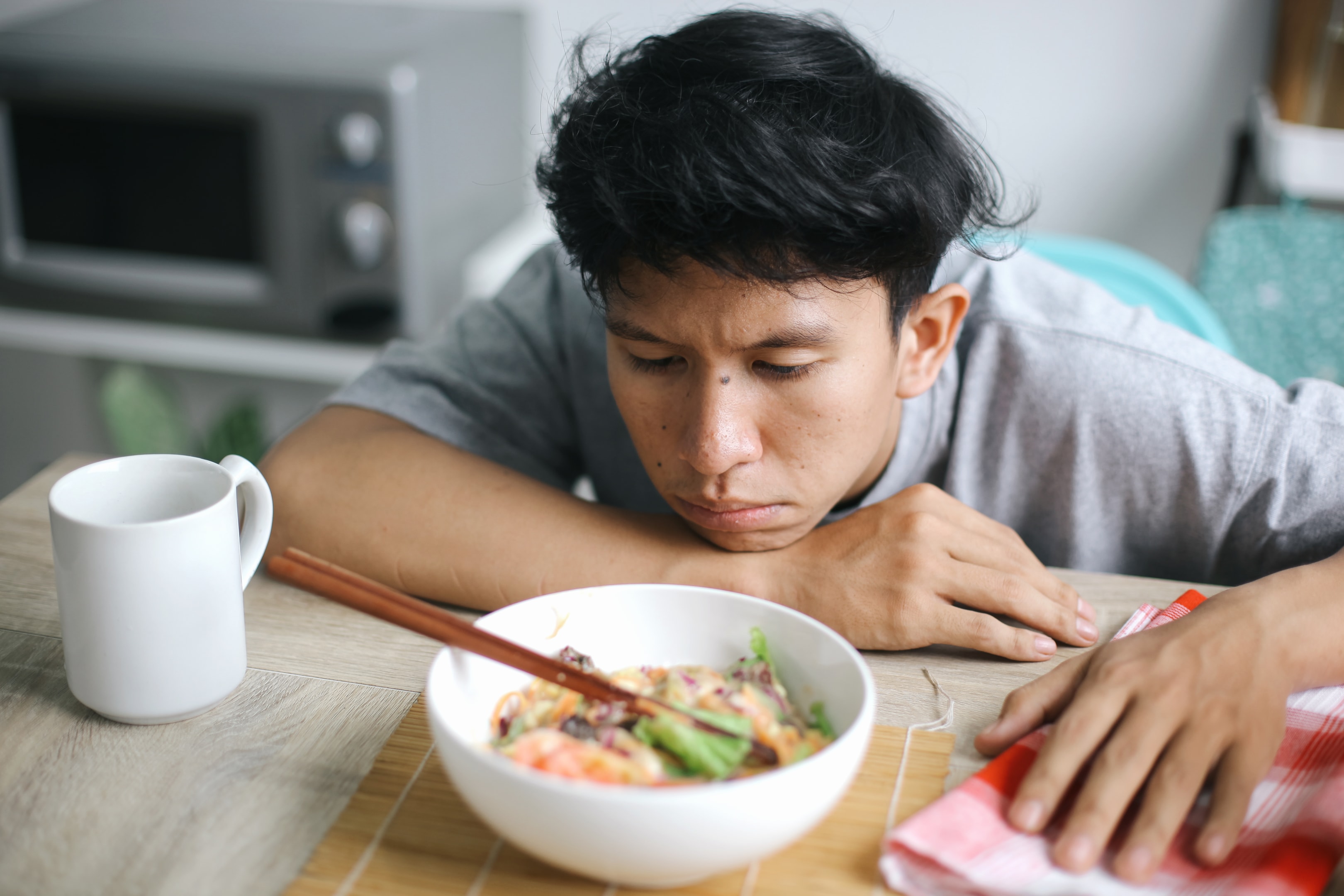A man looking down at a bowl of food with a somber and overwhelmed expression, representing the emotional challenges and internal distress associated with eating disorders in men.