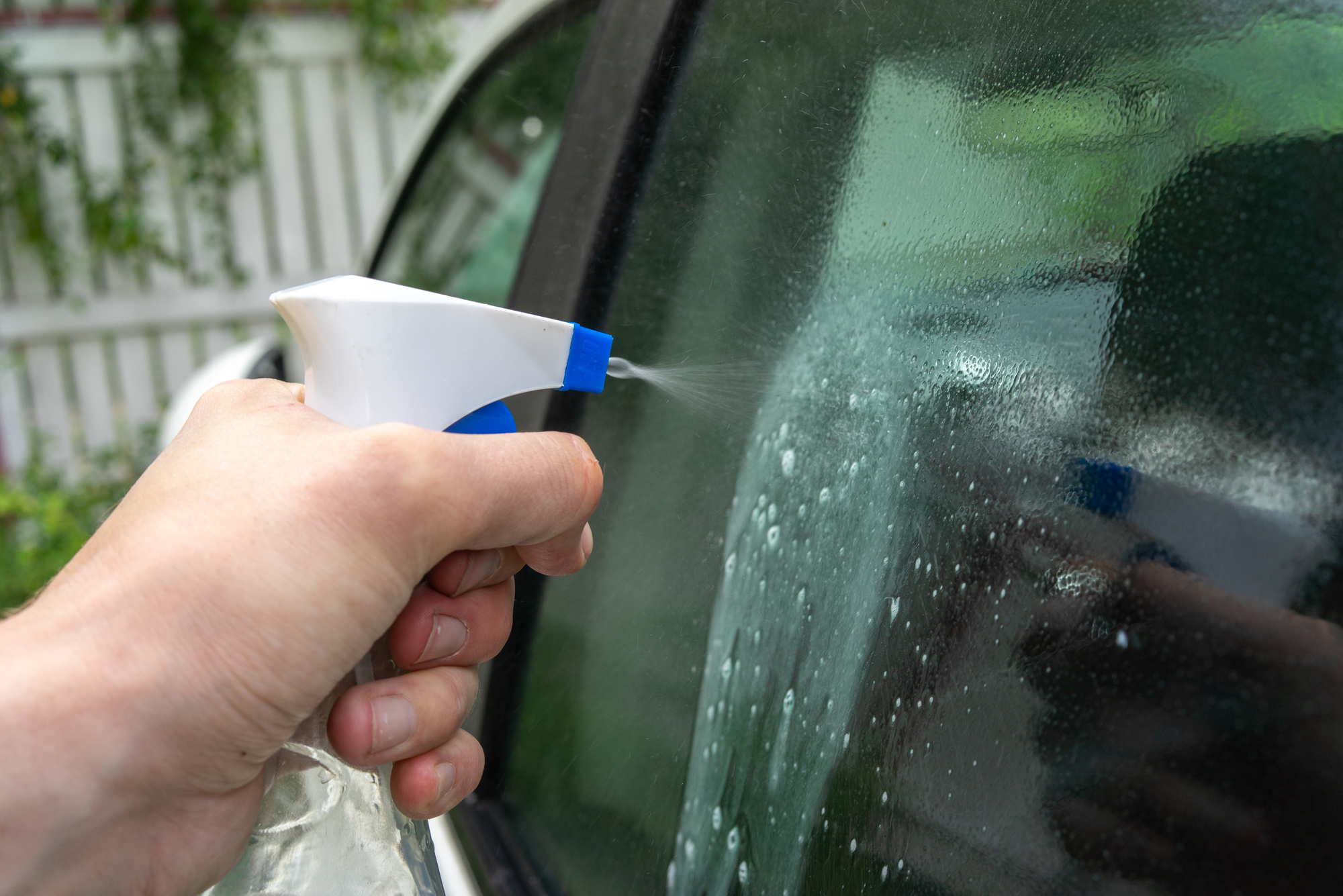 Hand spraying alcohol-based glass cleaner on car window