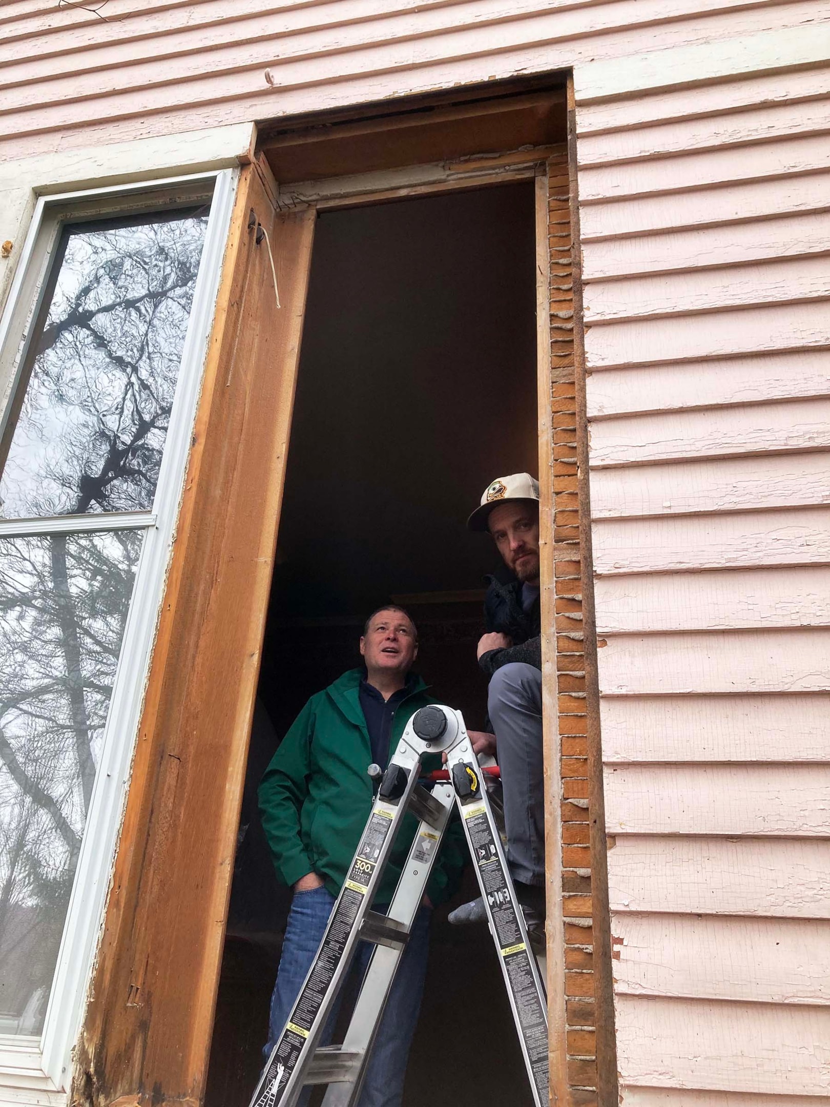 McClurg Remodeling crew members preparing a window opening during a historic window replacement project in Fayetteville, NY. Image shows partially removed frame on a late-1800s home with original siding and exposed lath.