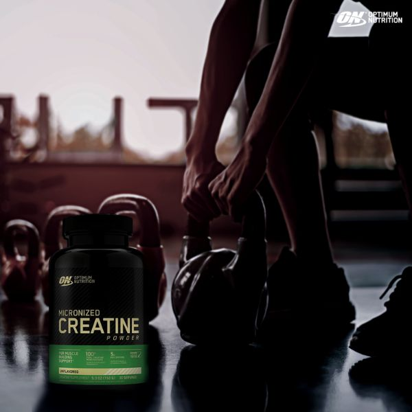 Creatina da Optimum Nutrition no canto esquerdo inferior da imagem e as mãos de um atleta segurando uma kettlebell. Imagem: site oficial da marca