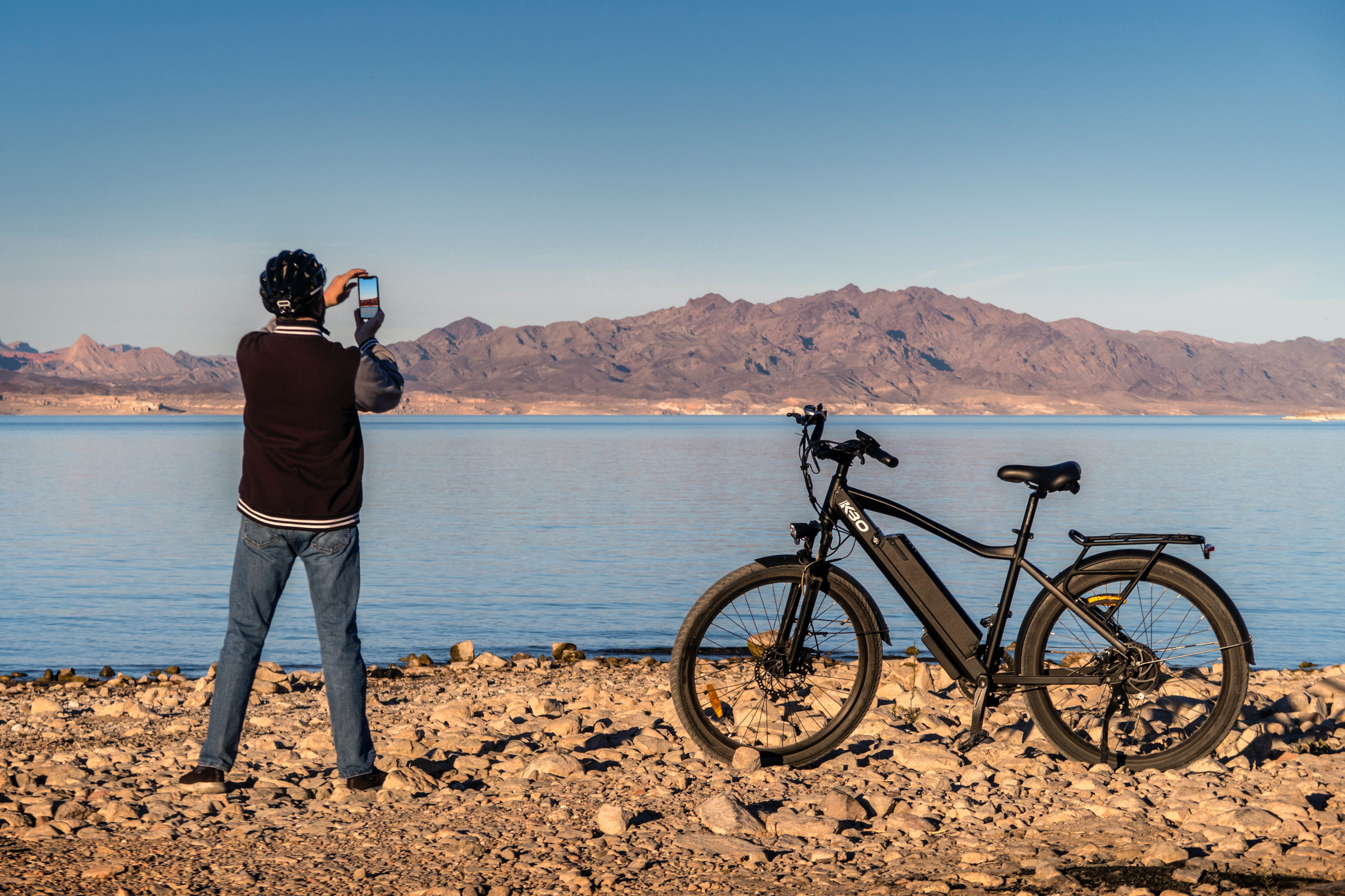 Homem tirando foto de sua ebike, com um lago e montanha ao fundo
