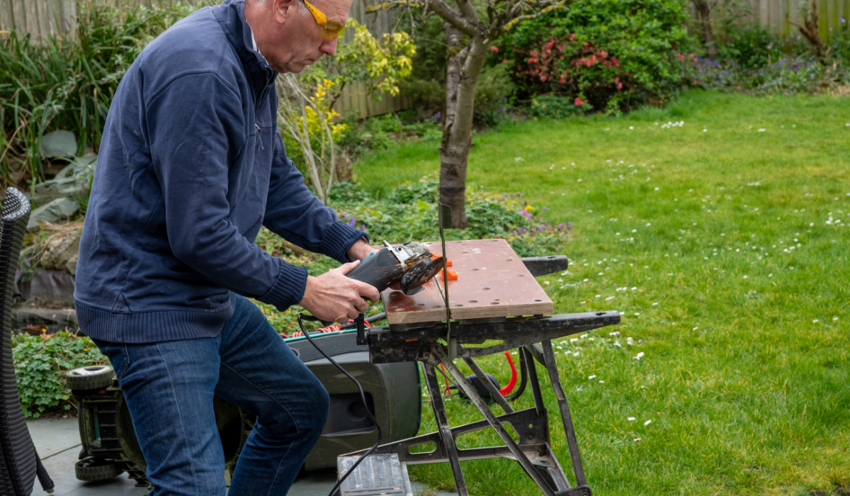 A figure woking in a graden at a work bench - using an angle grinder to sharpen a rotary mower blade