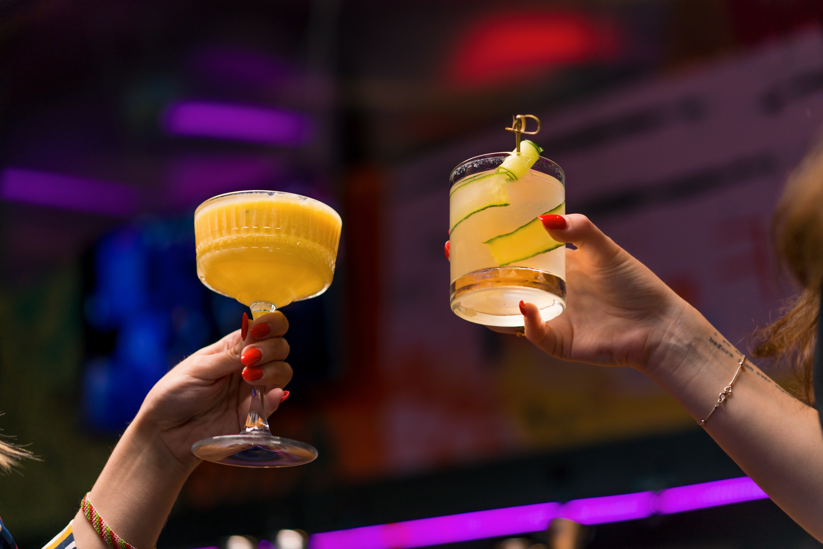 Two cocktails held in hands by guests at a bar.