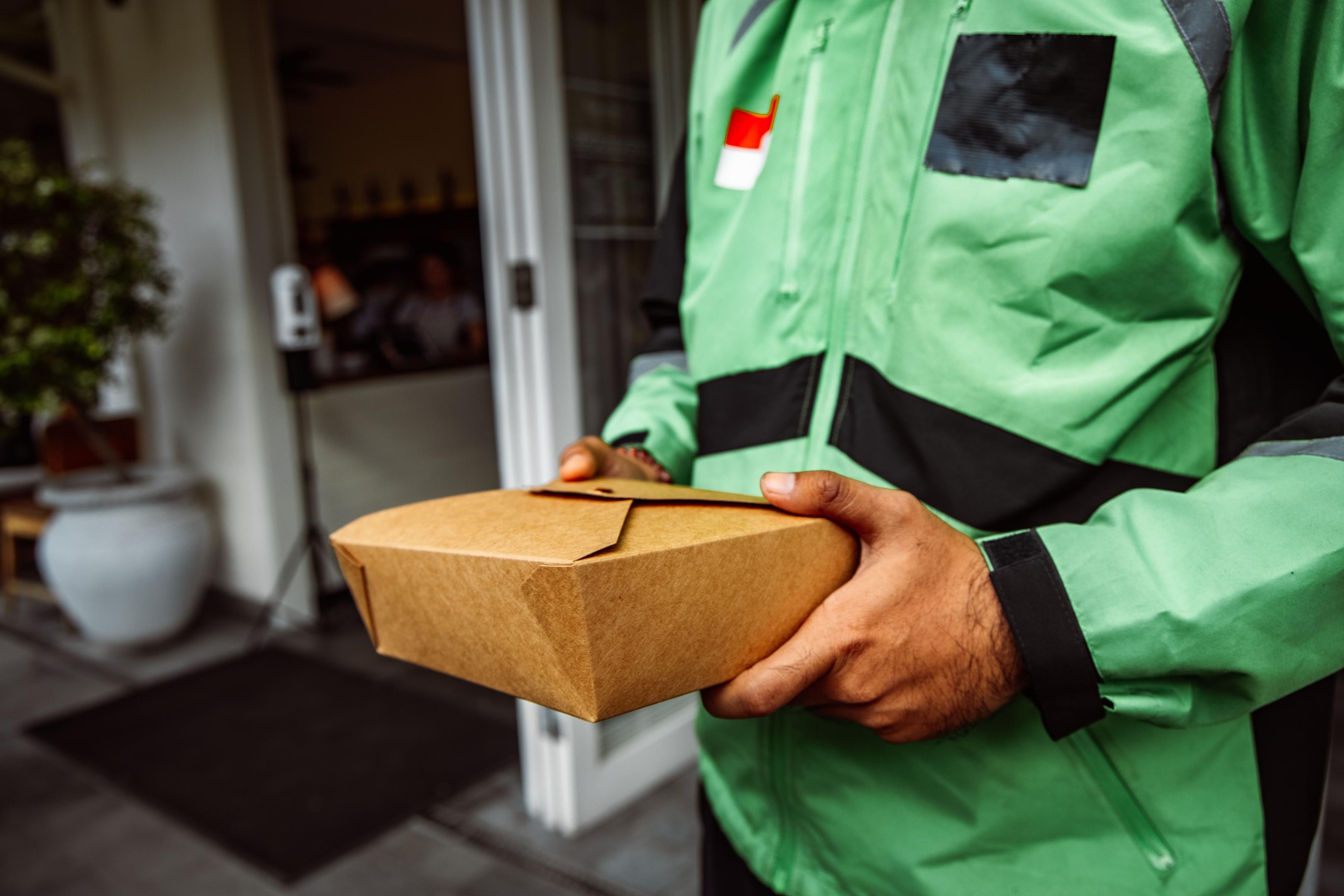 A happy customer stands at a restaurant counter, beaming as they receive a takeout bag from a friendly staff member, highlighting a positive customer experience.