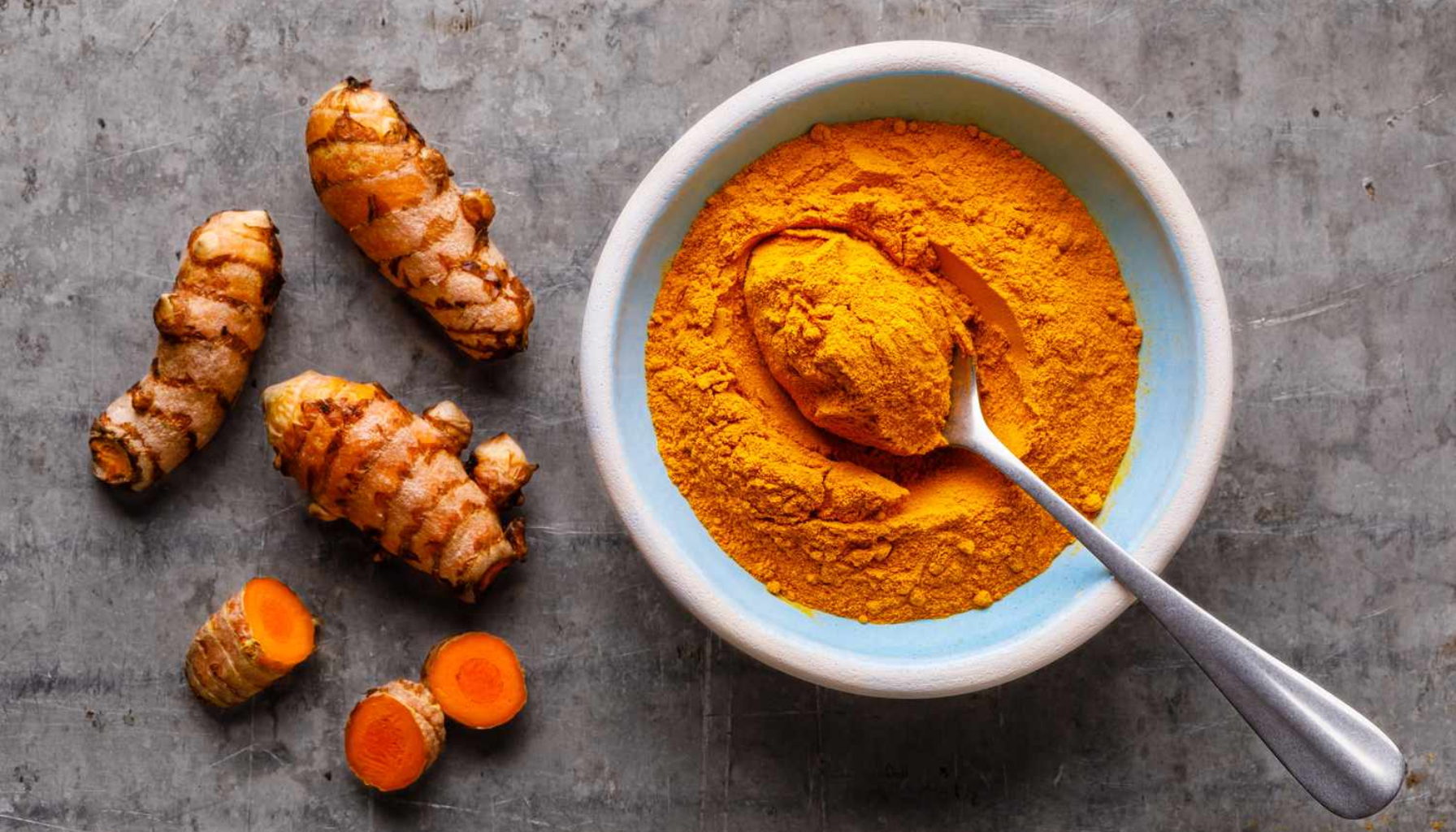 Sure Oppstøt og Tennene Dine: Den Usynlige Fienden i Magen 15 Rå fersk gurkemeie ved siden av en skål med malt gurkemeie på en grå steinbenk.