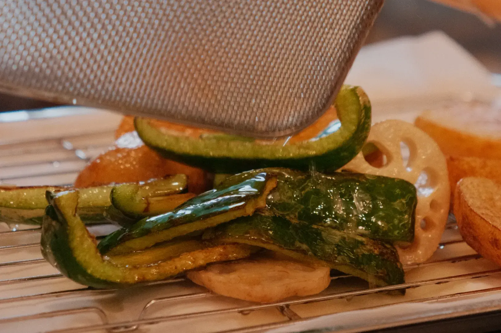 Close-up of toasted bread layered with glossy grilled green peppers and vegetables on a wire rack beneath a metal grill press; warm and appetizing.
