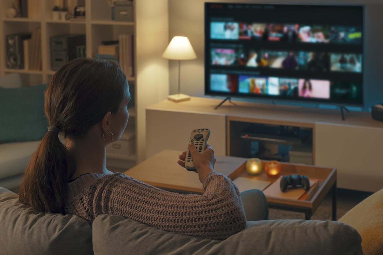 a woman holds a tv remote and browses a streaming service on her TV while sitting on the couch