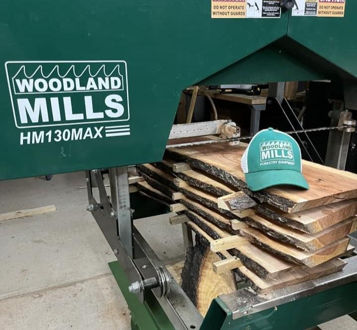 Une pile de planches recouverte d'autocollants sur le rail d'une scierie portable Woodland Mills HM130MAX, surmontée d'un chapeau.