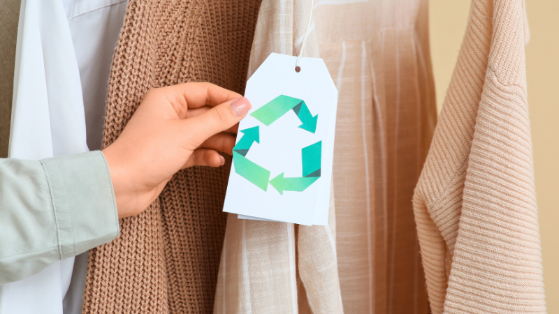 A person holding a green recycling symbol on a clothes hanger