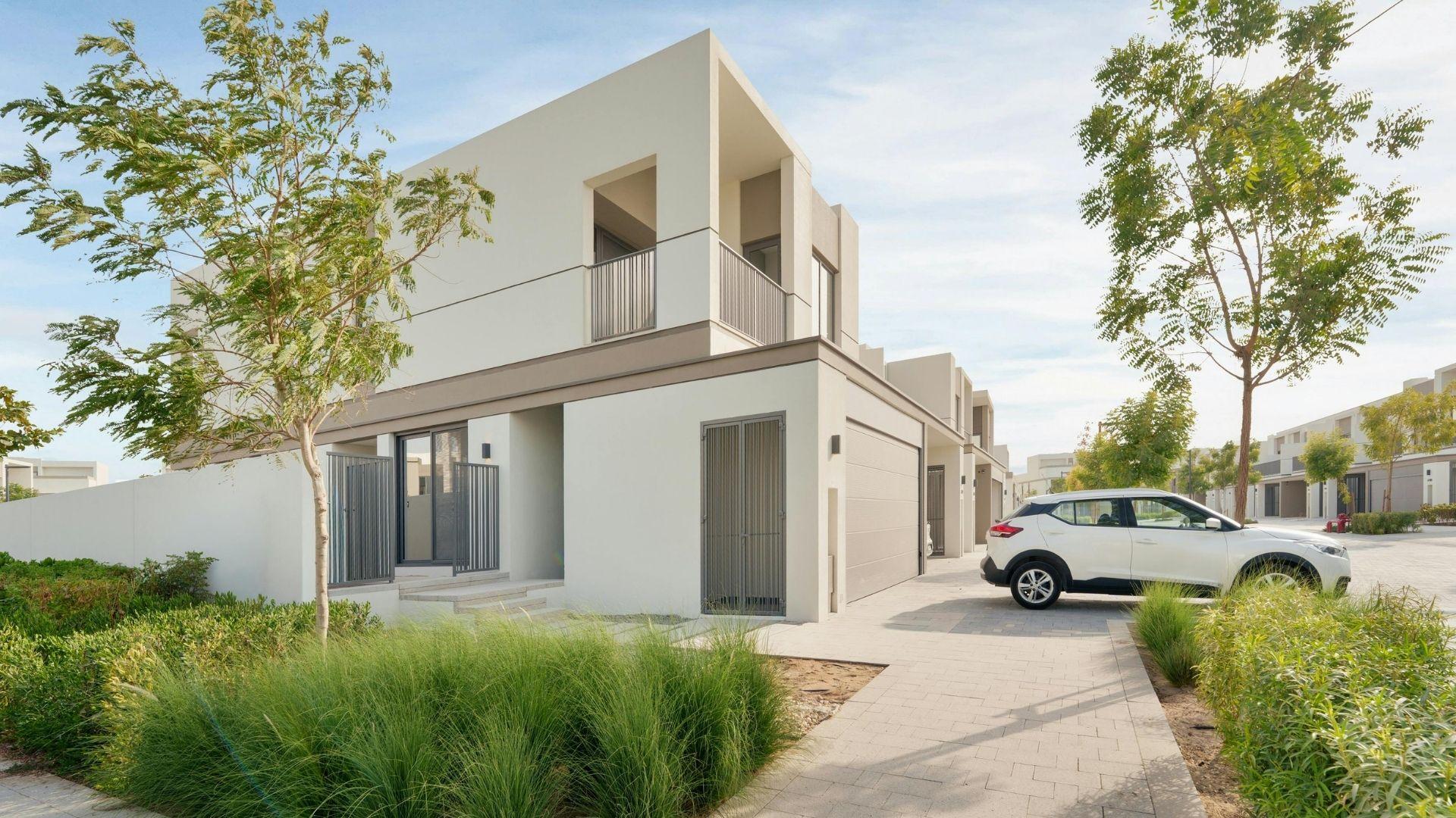 Modern two-story villa with minimalist white exterior, large windows, and a small front garden, featuring a driveway with a parked car and landscaped greenery.