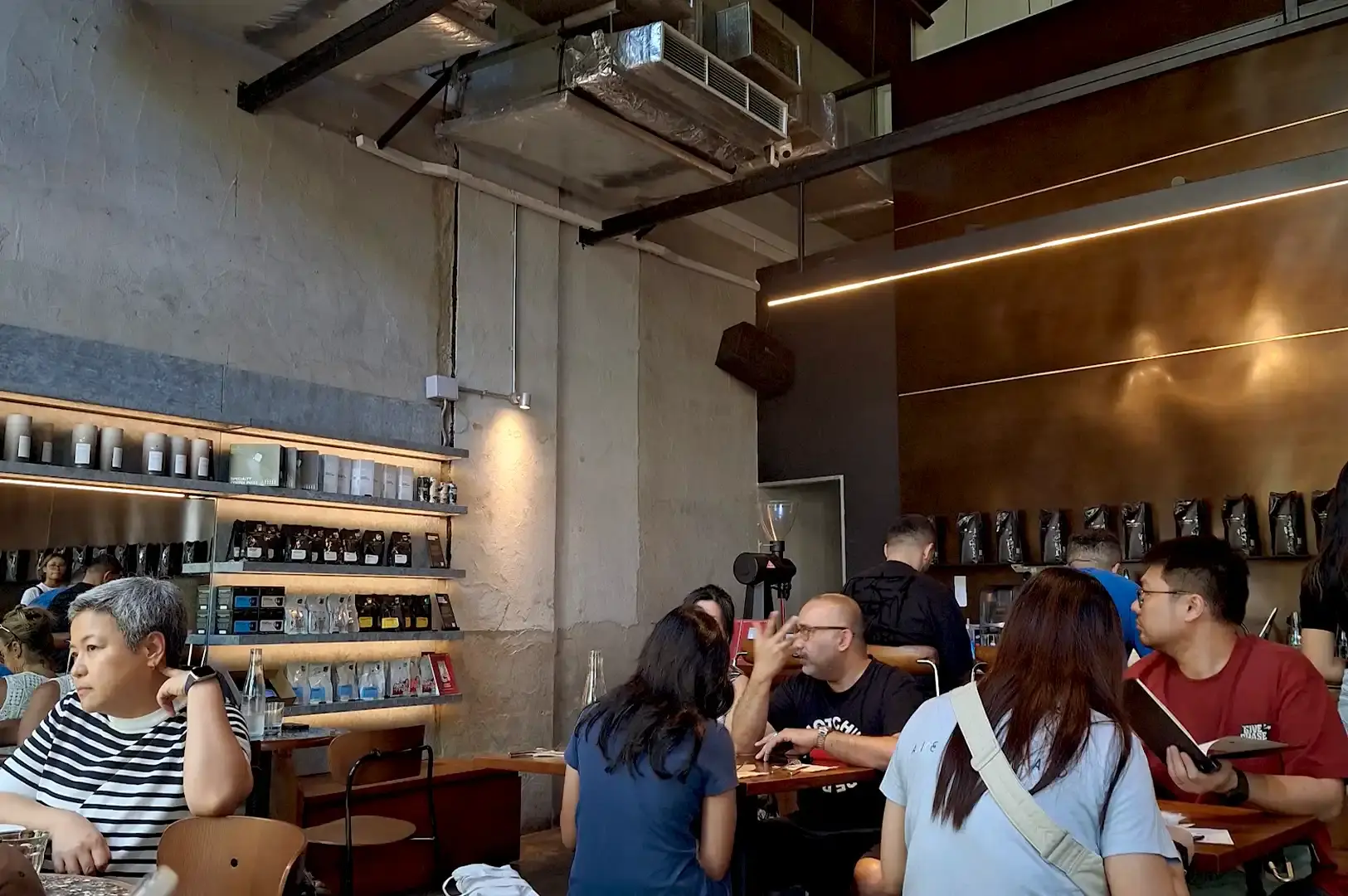 "The cozy interior of Toby's Estate Coffee Roasters showcasing industrial decor, retail coffee shelves, and customers dining.
