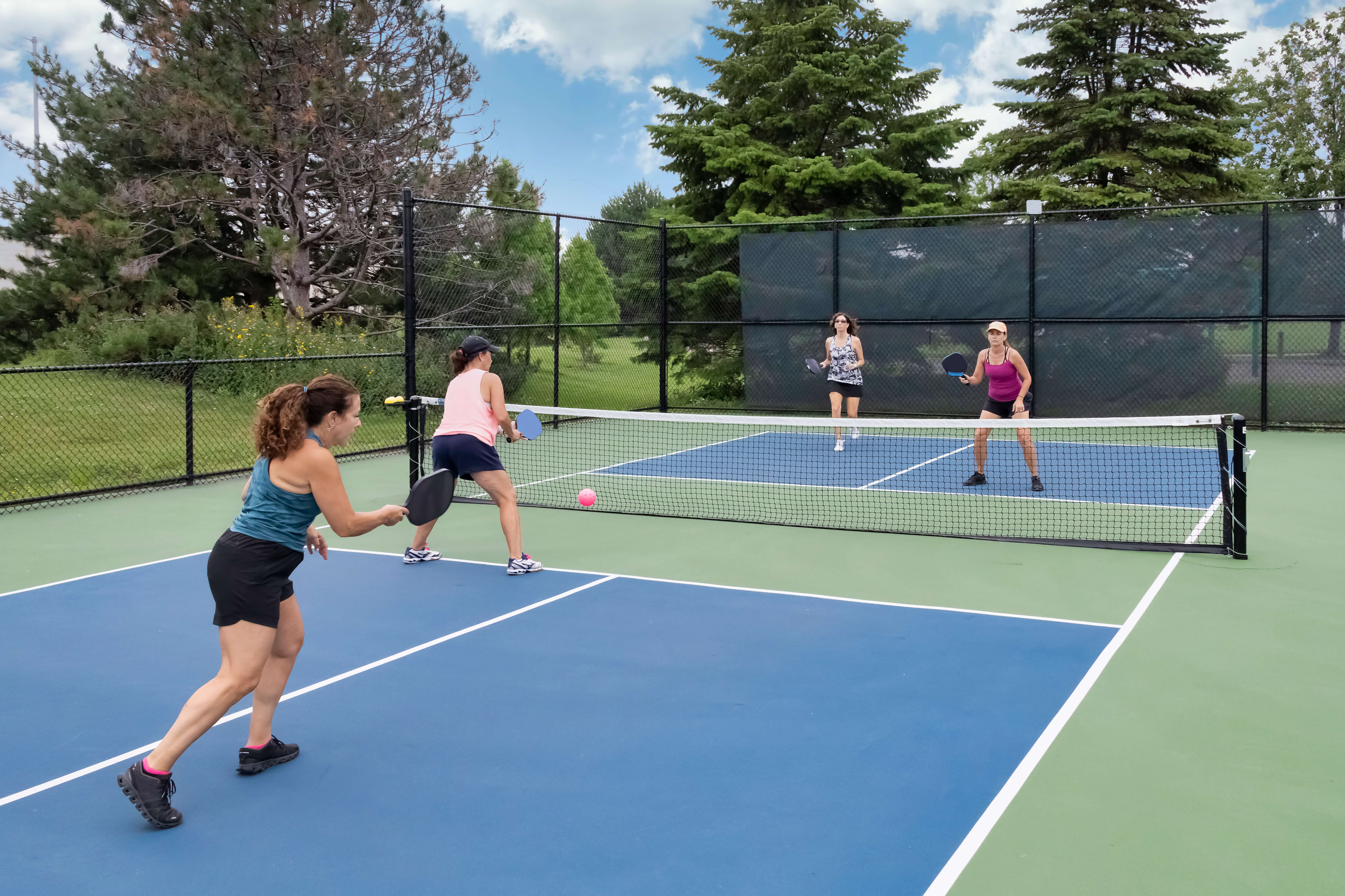 Four diverse women paired into two teams engaging in a pickleball match.