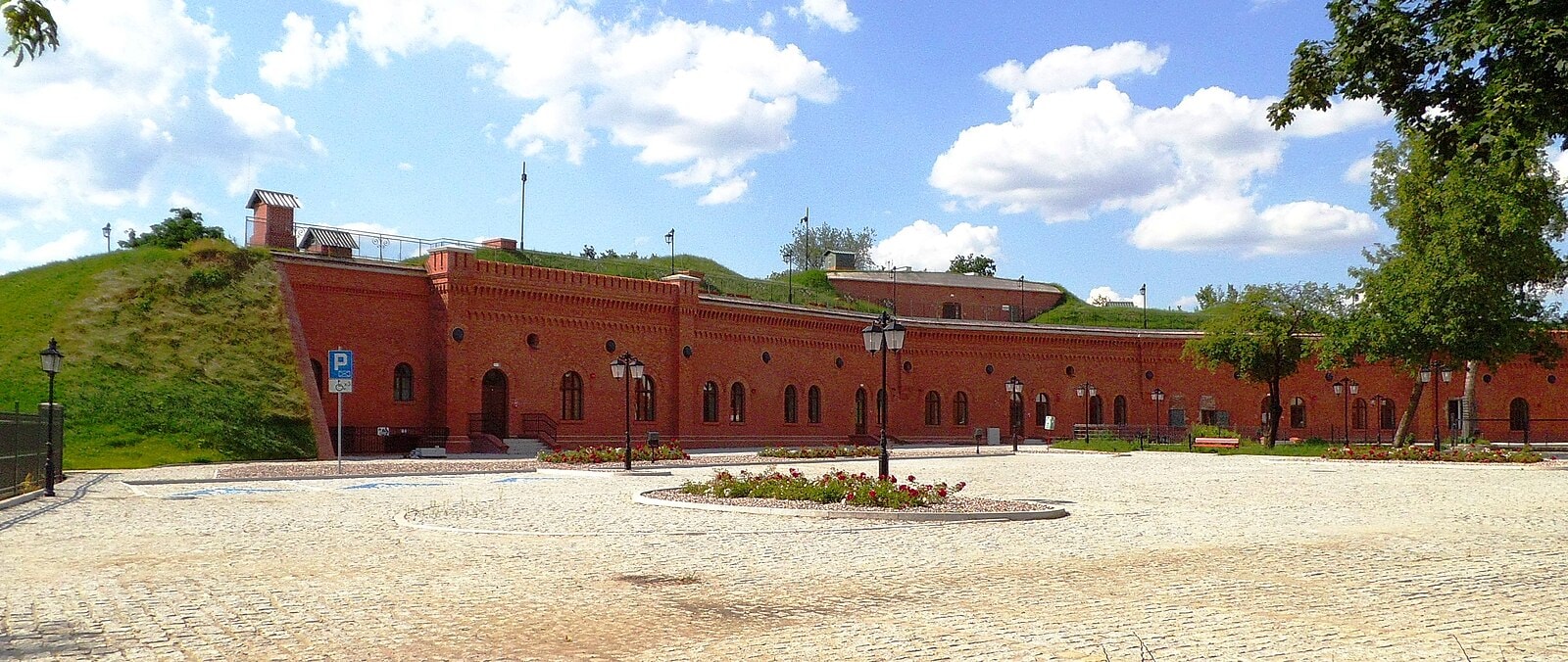 Rozległy i niski budynek z czerwonej cegły, który należy do Muzeum Twierdzy Toruń. Źródło: https://commons.wikimedia.org/wiki/File:Muzeum_Twierdzy_Toru%C5%841.jpg