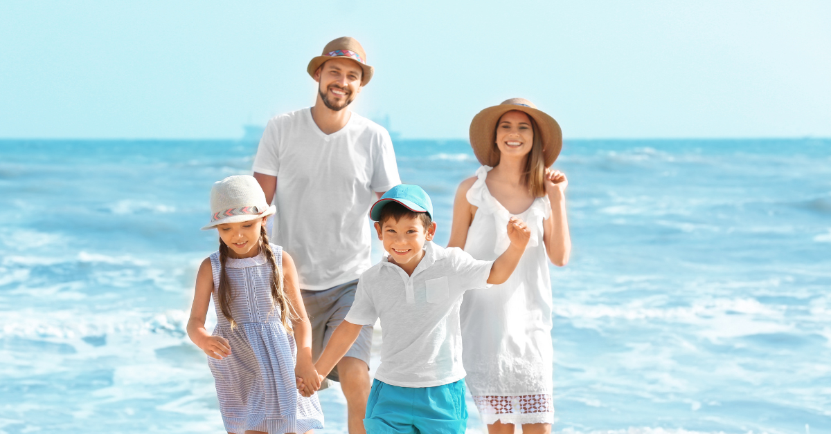 A smiling family of four walking along the Atlantic City beach near the shoreline on a bright sunny day.