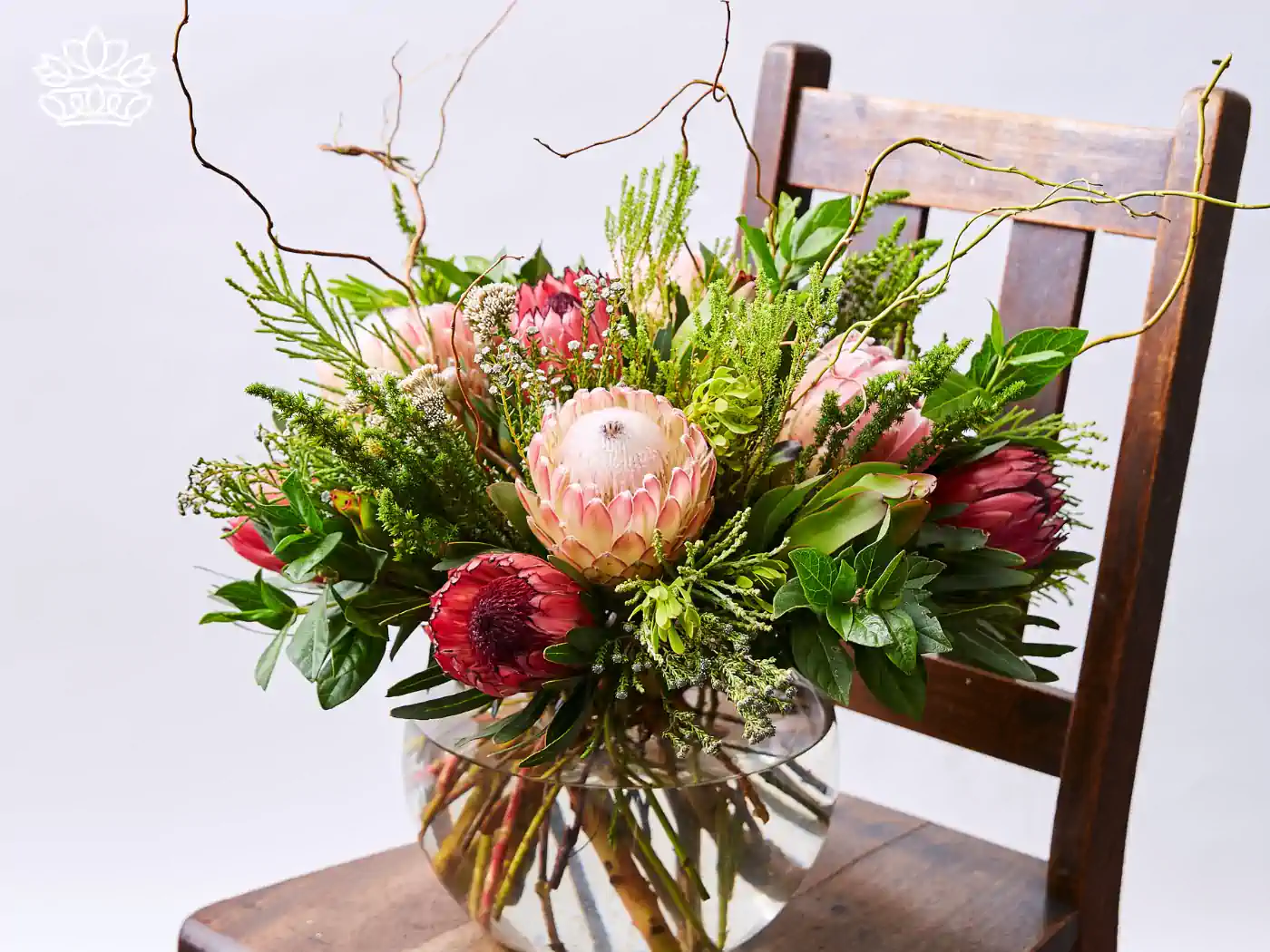 Stunning floral arrangement in a clear vase, featuring garden-fresh proteas and vibrant greenery, captured in a detailed photo. Fabulous Flowers and Gifts.