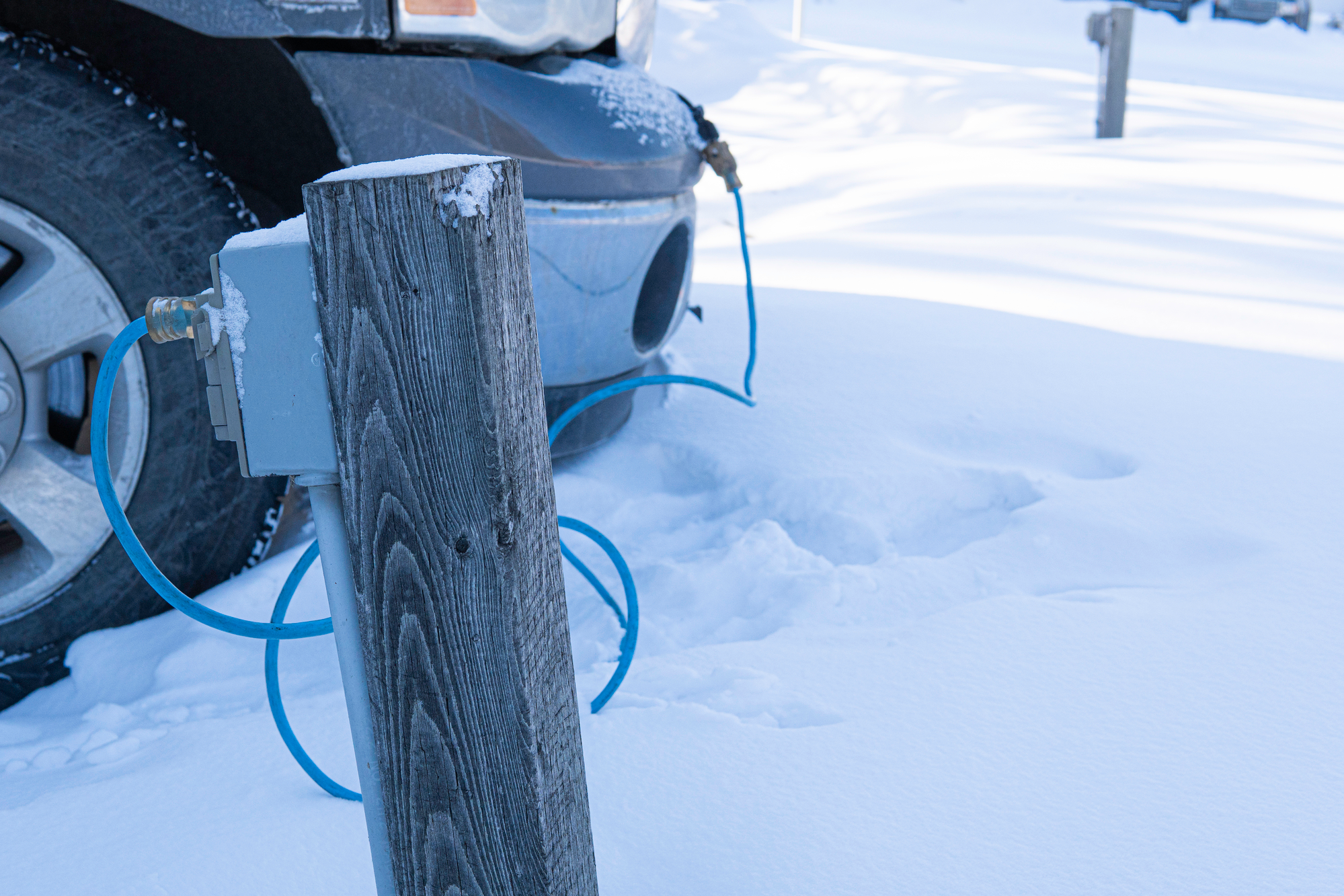 Wood pole with electric outlet, car is plugged in on background