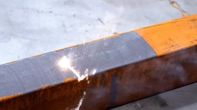 Laser cleaning beam removing paint from an orange metal beam.