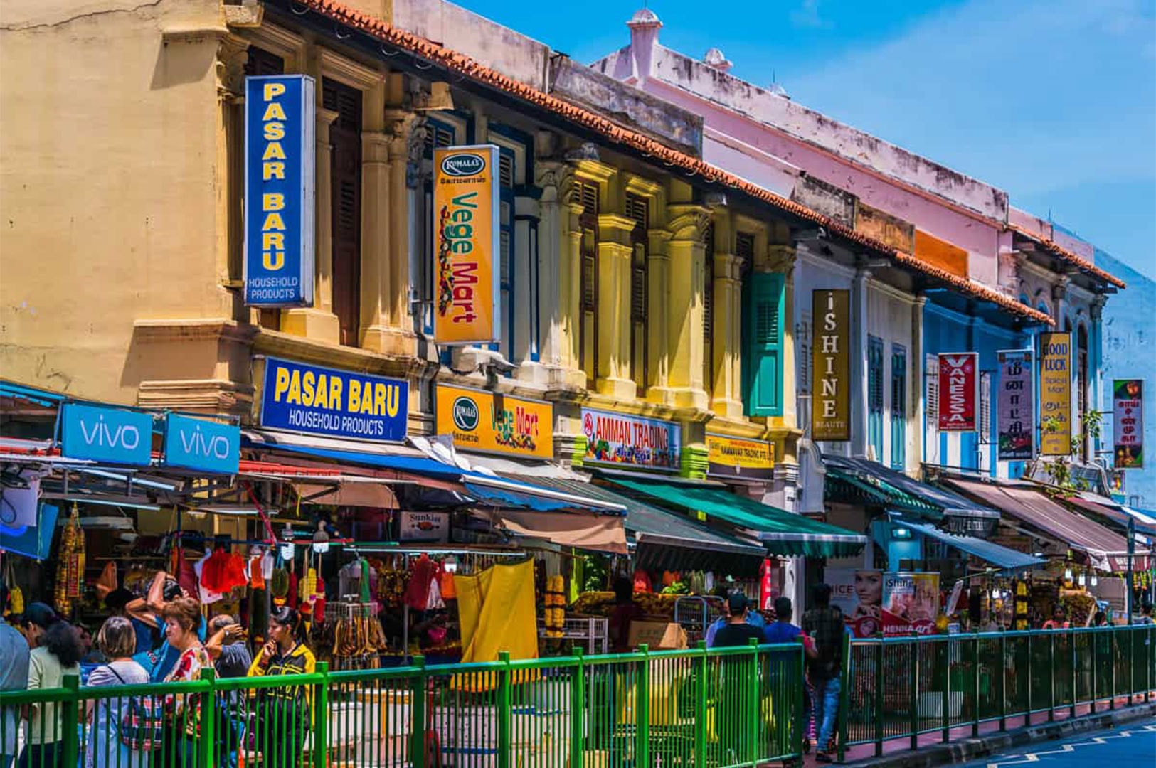 Colorful traditional shophouses lining a street in the Kampong Glam/Arab Street area of Singapore, with market stalls below.