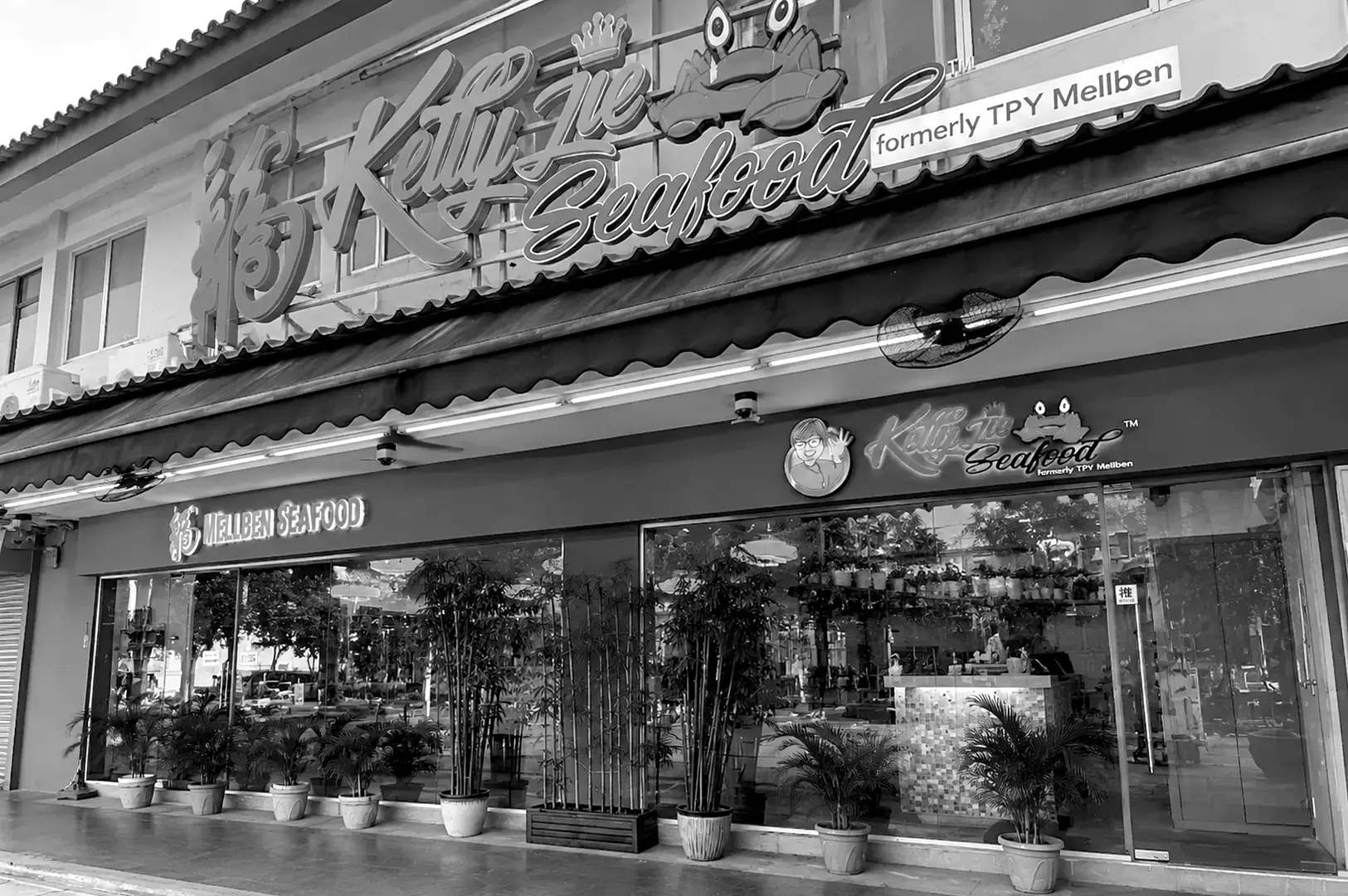 Front exterior of Kelly Jie Seafood restaurant showing its prominent signboard, glass storefront, potted plants, and spacious dining area visible through the windows.