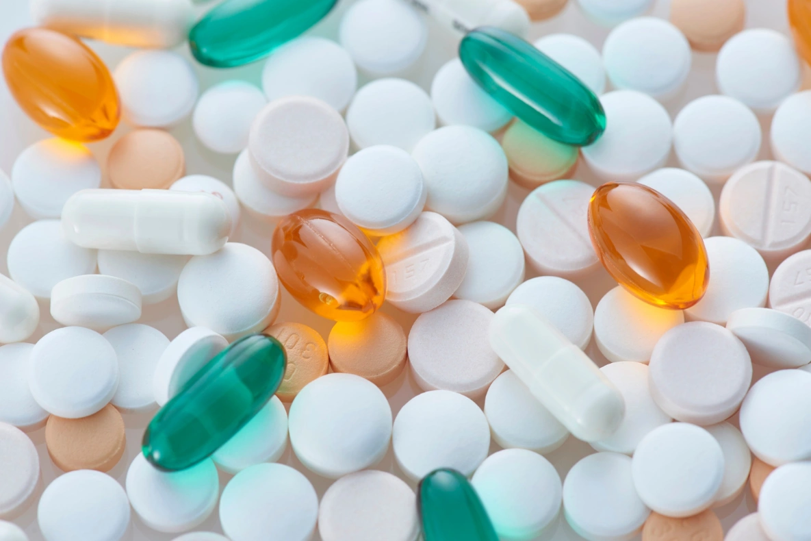 An assortment of pills and capsules in white, orange, and green.