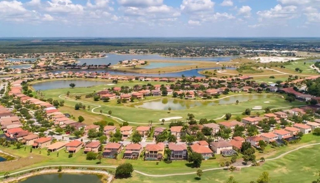 An aerial view of the Valencia Country Club showcases its pristine golf course and the surrounding residential homes nestled within lush landscaping, highlighting the vibrant and welcoming community atmosphere of this premier gated community in Naples. The image captures the resort-style pool and well-maintained grounds that enhance the luxurious lifestyle offered in this esteemed country club.