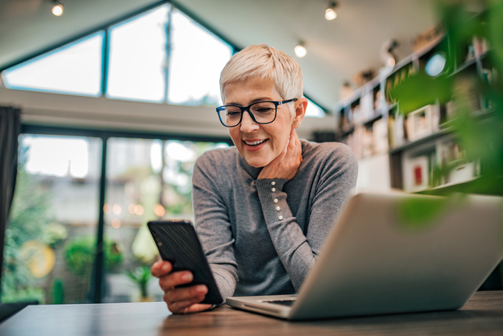 Short haired blond woman with glasses doing research on her cell. 