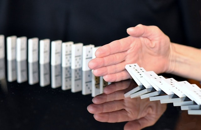 Dominoes falling and a hand stopping them