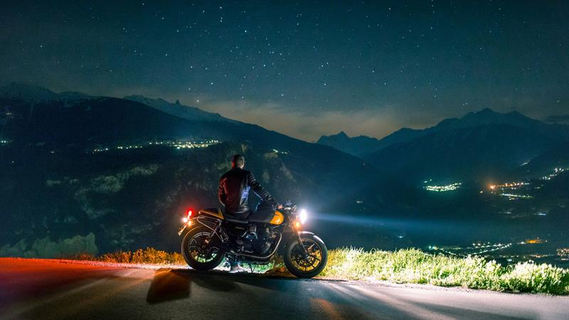 Man on a motorcycle with bright lights on a hill road at night.