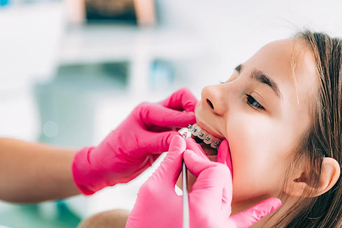 A dental professional in pink gloves adjusting a patient's braces during a routine orthodontic procedure.