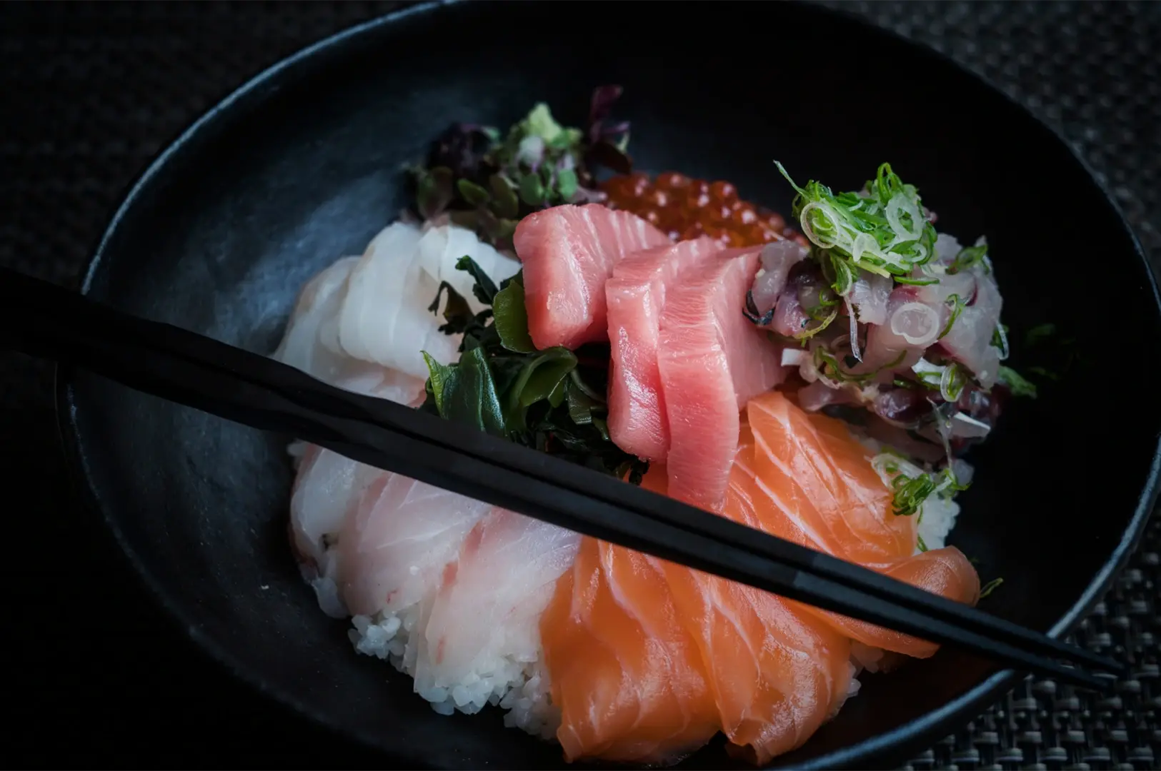 A chirashi bowl filled with assorted raw fish and roe over sushi rice, with chopsticks resting on top.
