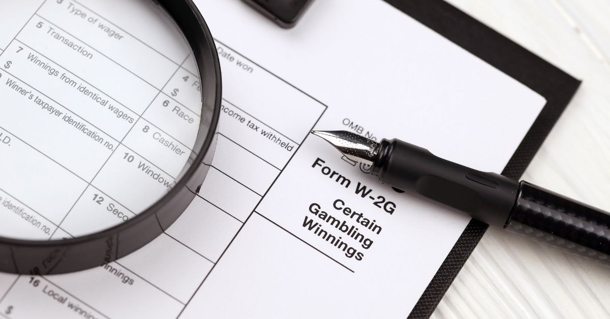 Close-up of Form W-2G document, pen, and magnifying glass for reviewing gambling winnings.