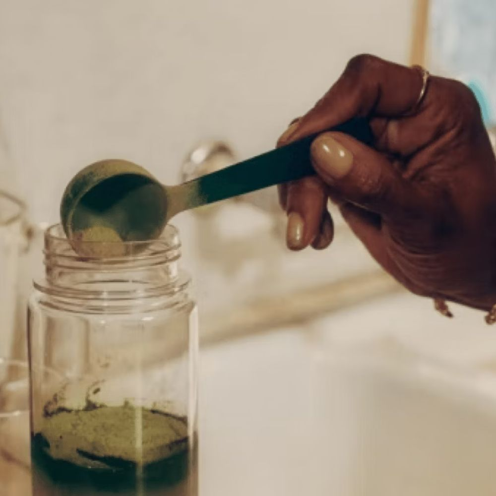 A person scooping Athletic Greens into their shaker bottle