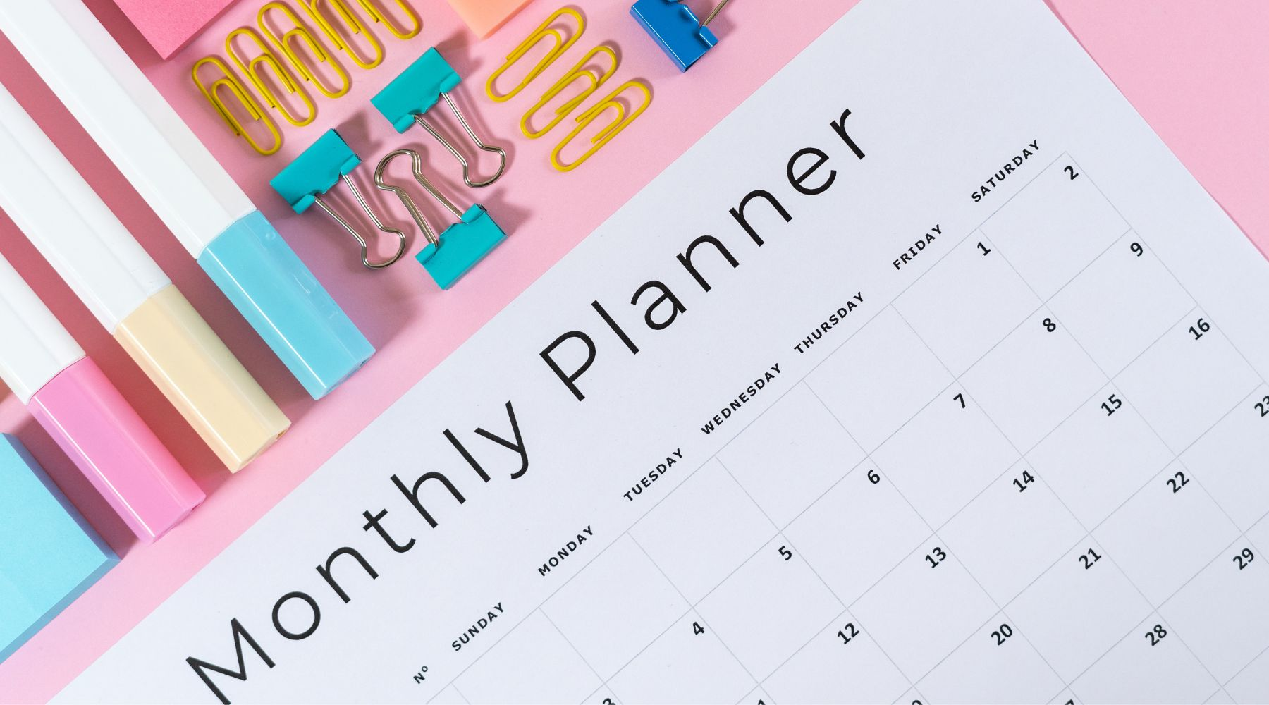 Monthly planner showing the first month with colorful paper clips and highlighters on a pink surface.