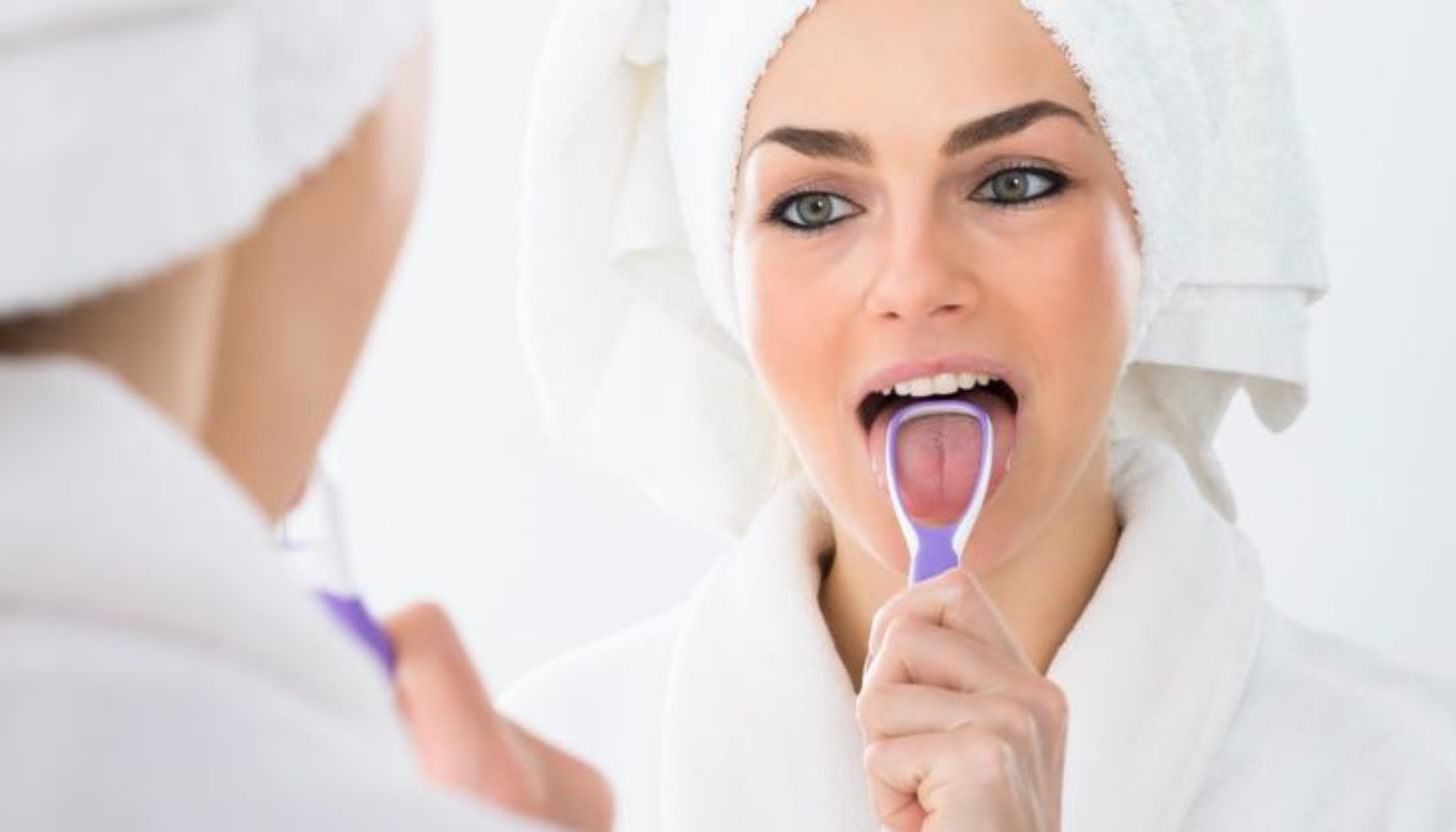 Tungehelse: Hva Tunga Forteller om Kroppen Din 17 Kvinne rengjør tungen med tungeskrape foran speilet, som del av daglig munnpleierutine.