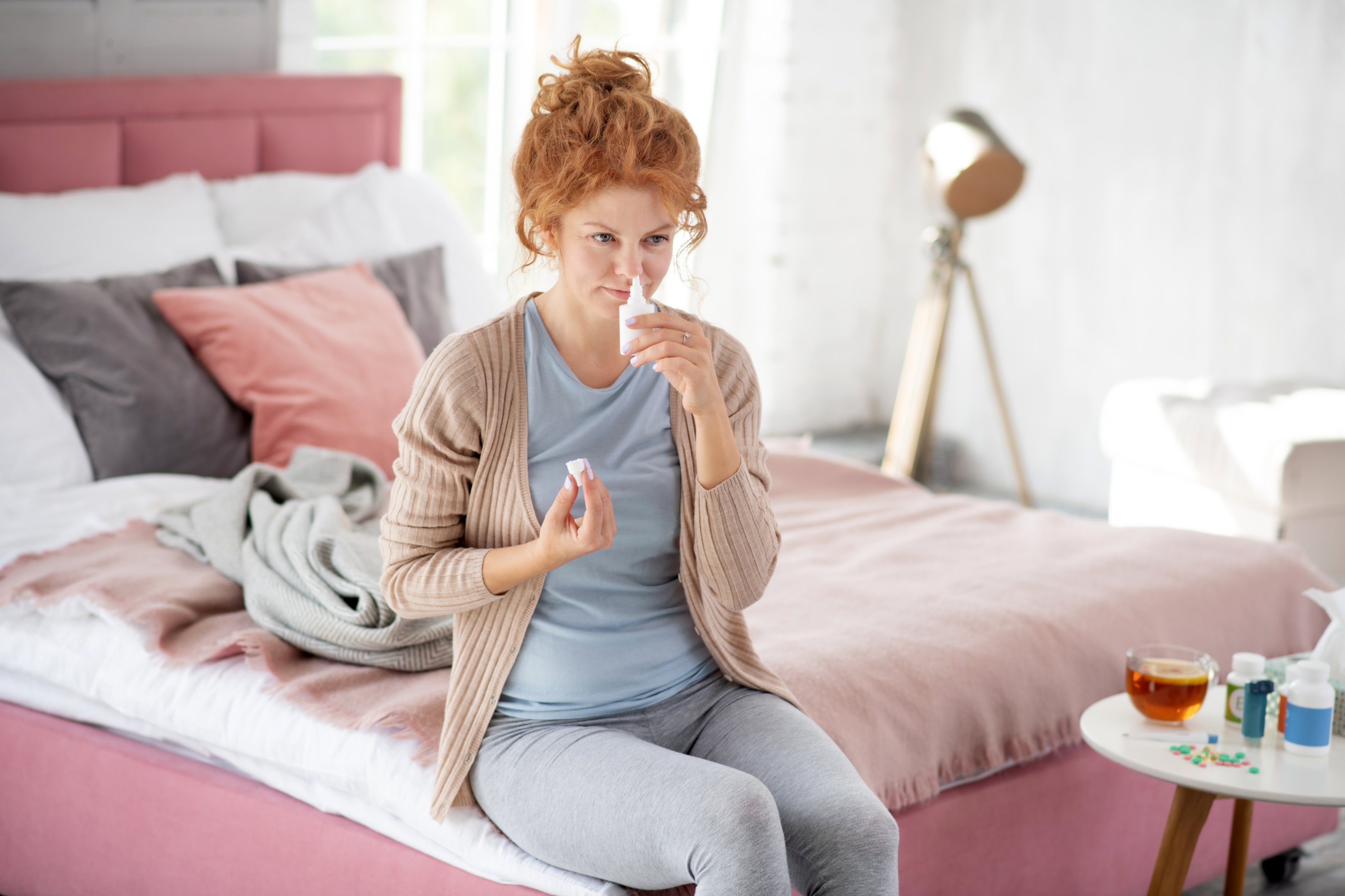 An image of a congested women spraying nasal spray into her nose. 