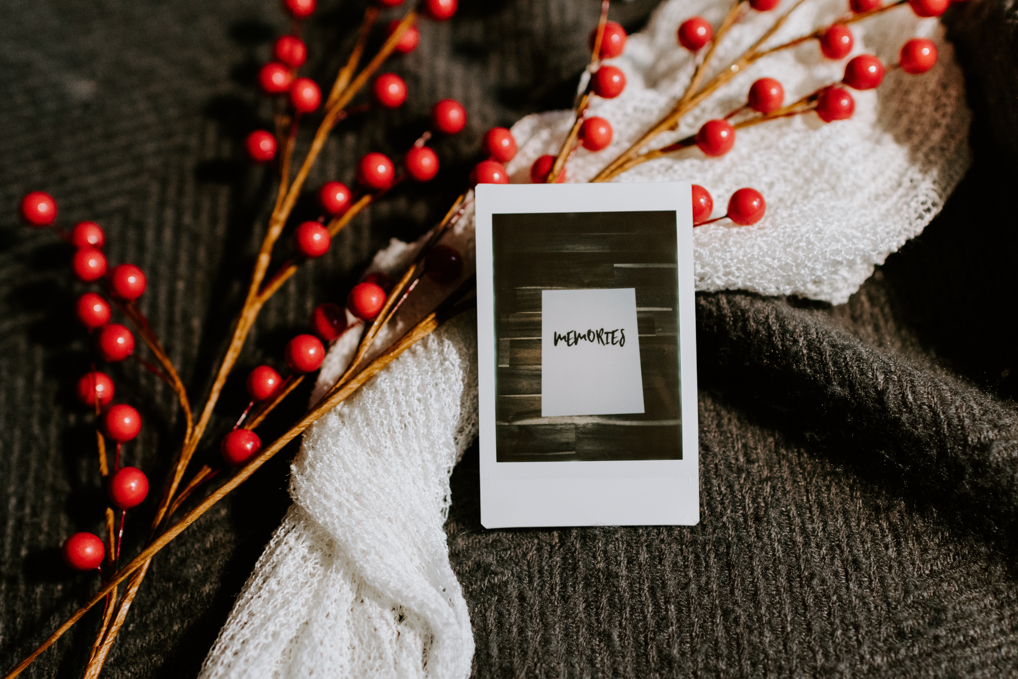 A holly branch on top of a white scarf and a Polaroid of a page that just says memories.