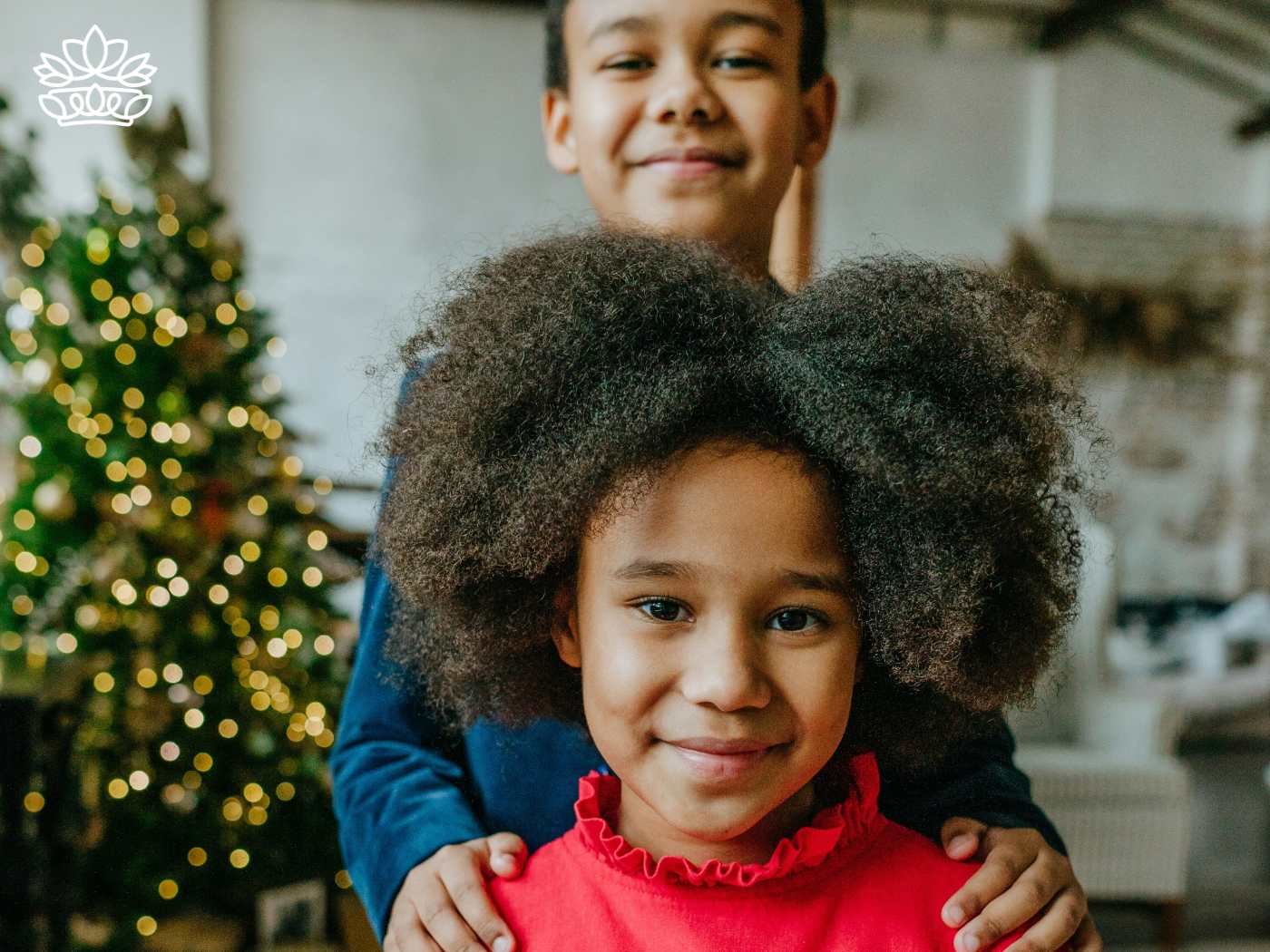 Joyful siblings with a sparkling Christmas tree in the background, capturing the essence of family festivities, from Fabulous Flowers and Gifts.