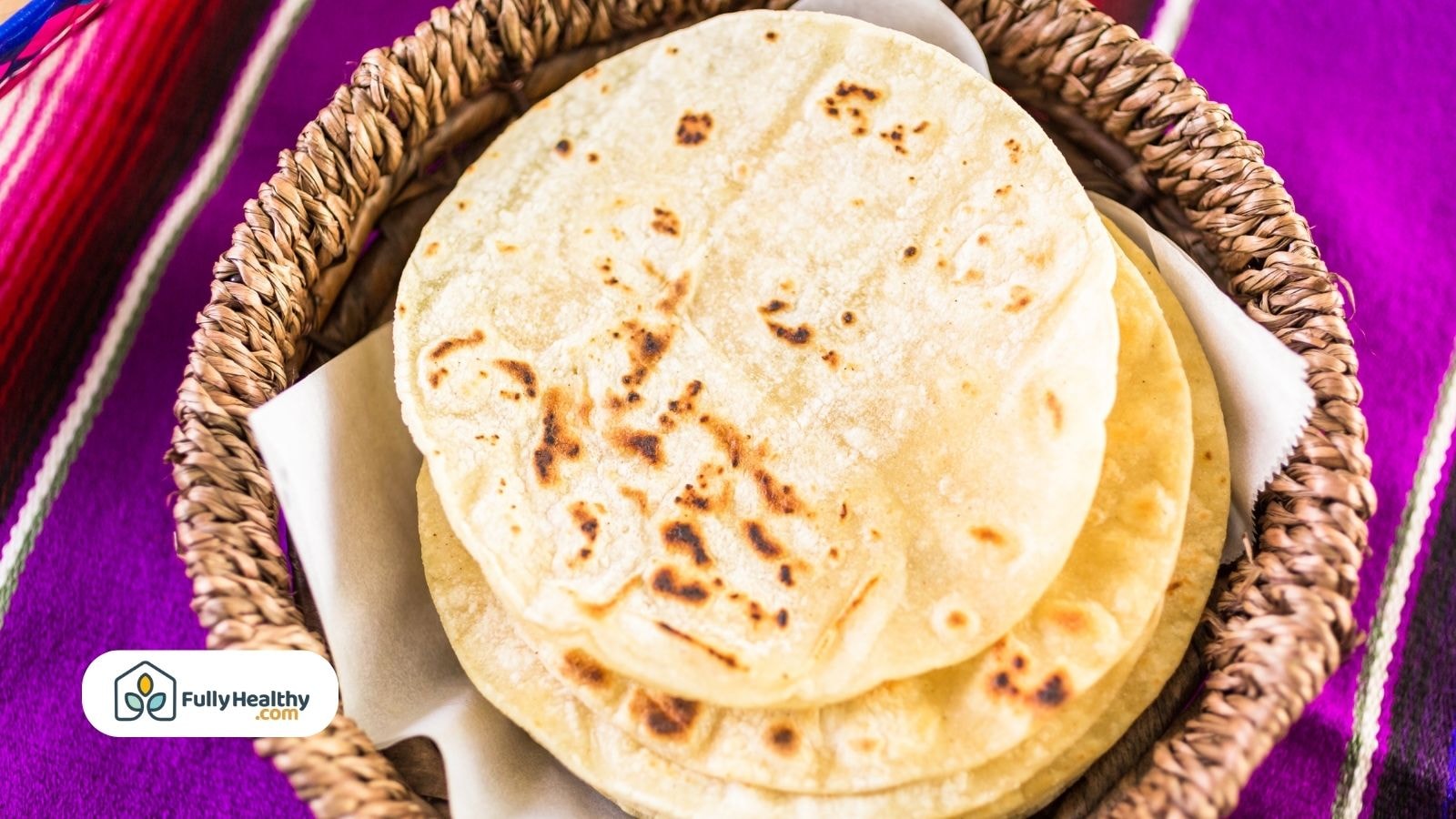 Stack of flour tortillas in a woven basket on colorful cloth