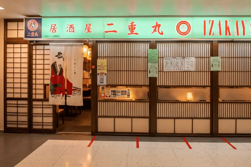 The storefront of Izakaya Nijumaru, featuring a bright green sign, traditional wooden lattice sliding doors, and a white noren curtain depicting a traditional Japanese figure.