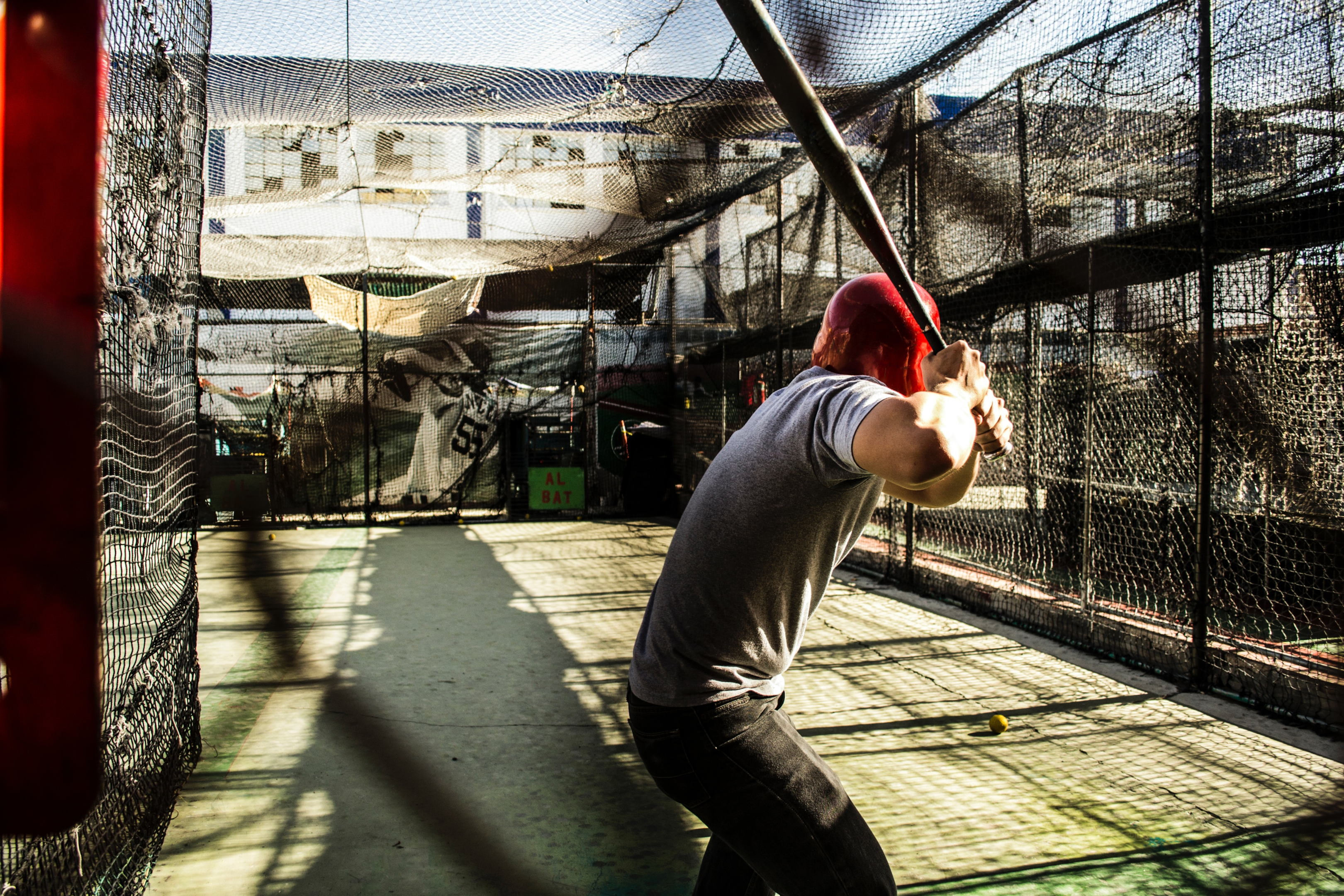 A baseball player in the batting cage with a wood baseball bat in his hands.