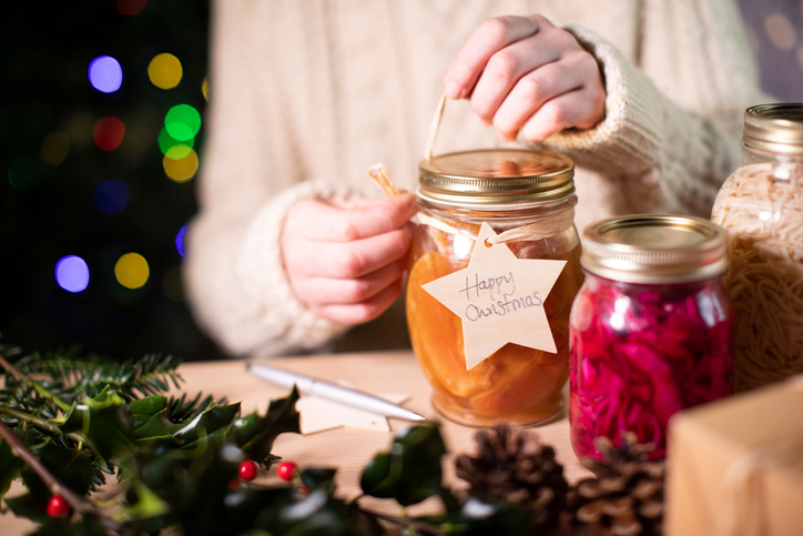 Woman tying a bow around a homemade gift of a jar of jam. 