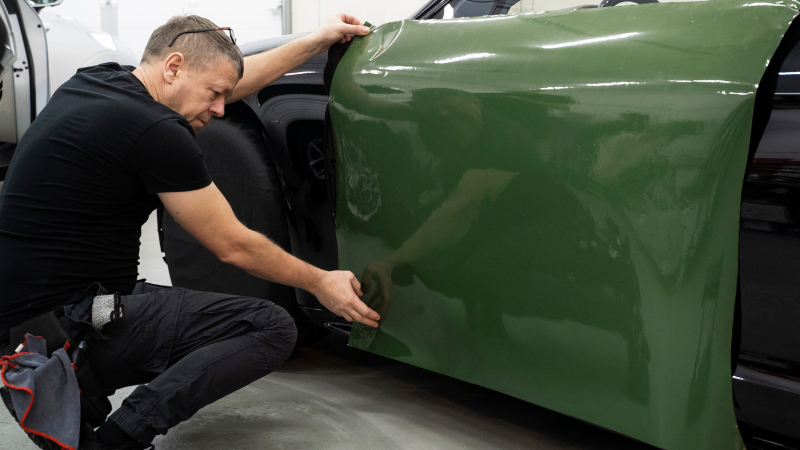 A mechanic is applying Drape film over the car to give it a new look.