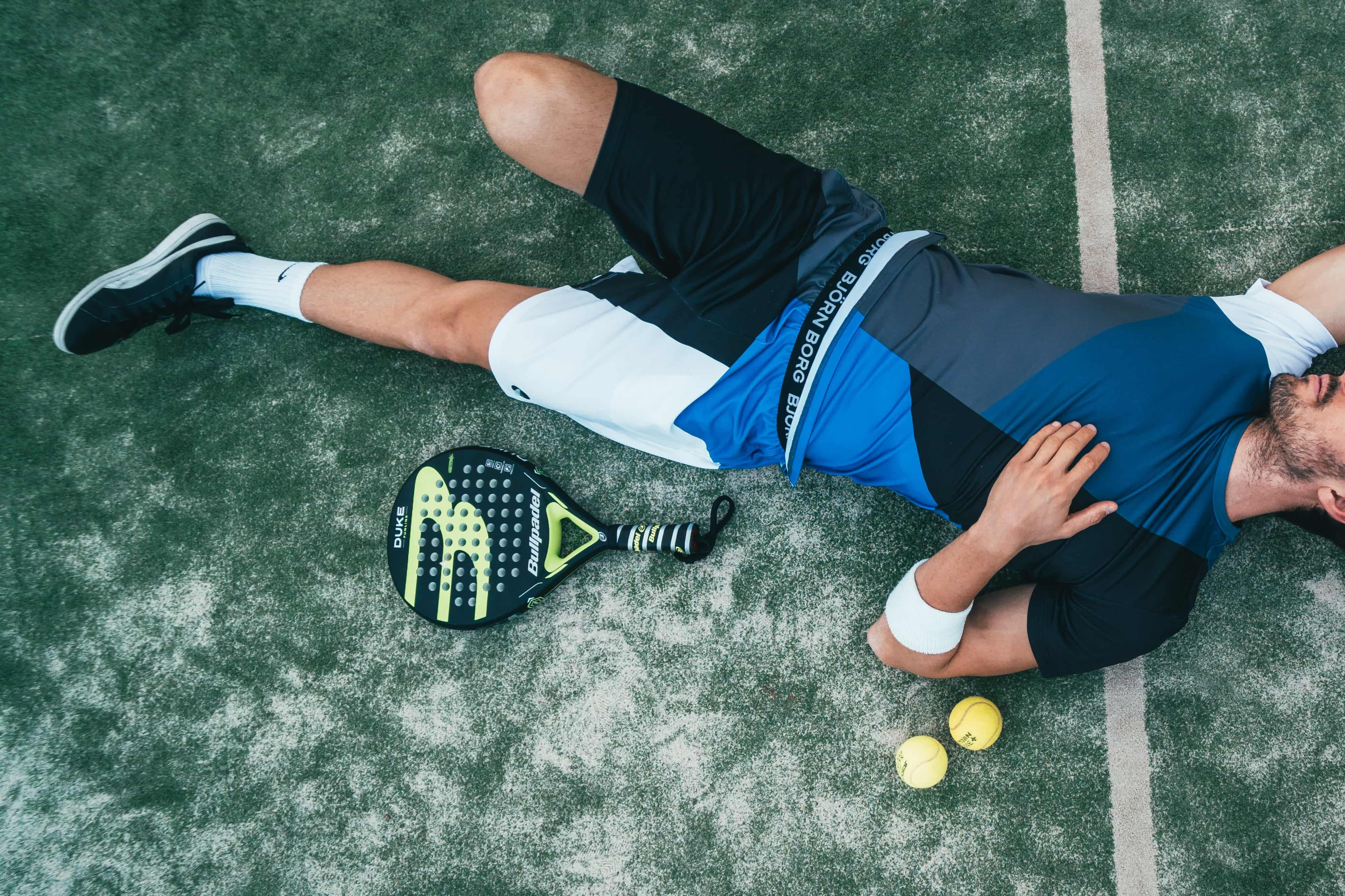 jouer de padel couché sur le terrain avec une raquette et des balles
