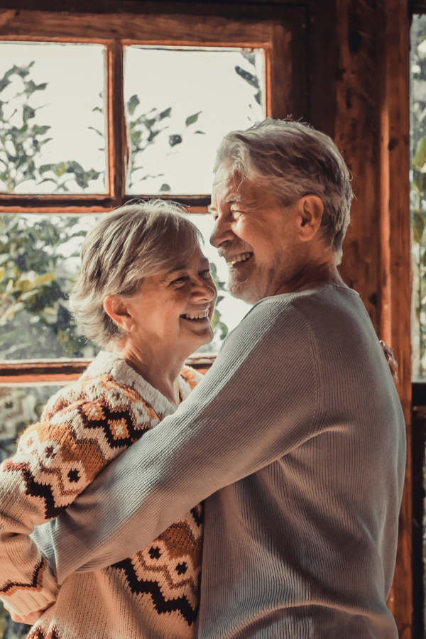 an older couple embrace in front of a window