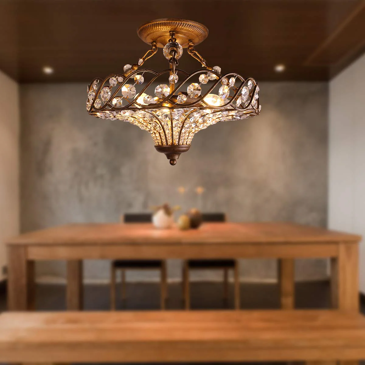 Antique brass semi-flush mount chandelier hanging above a wooden dining table and chairs, set against a blurred backdrop, enhancing the dining room ambiance.