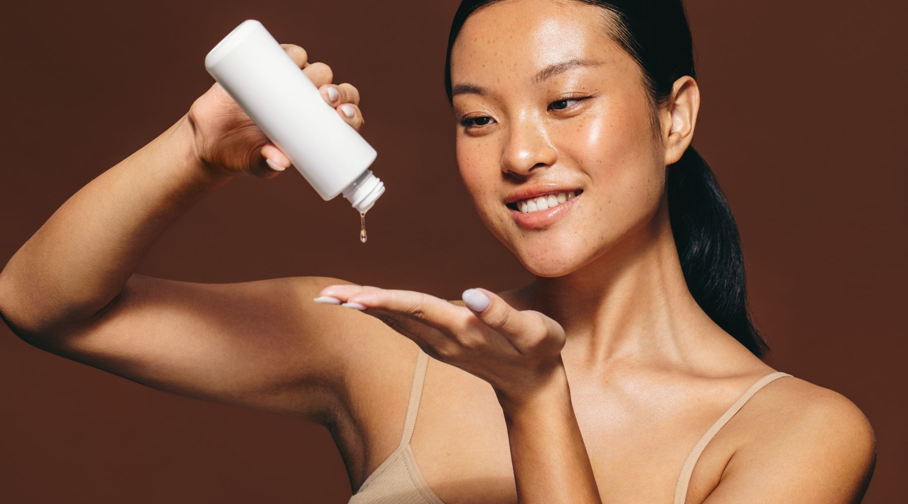 Asian woman applying serum to arm from a white bottle