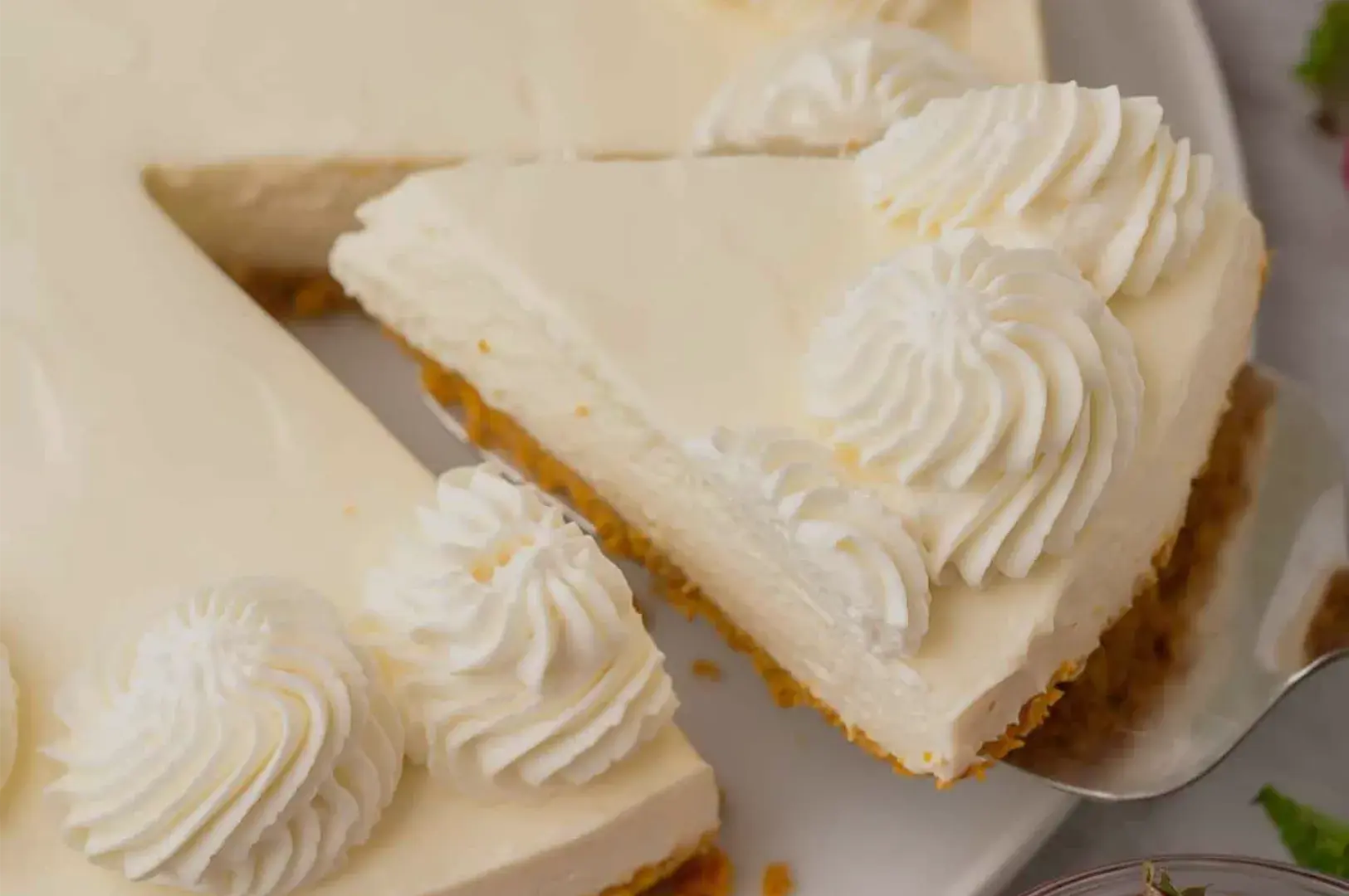 A slice of white-frosted cake, decorated with piped cream rosettes, rests on a spatula above another piece, creating an elegant, indulgent dessert scene.