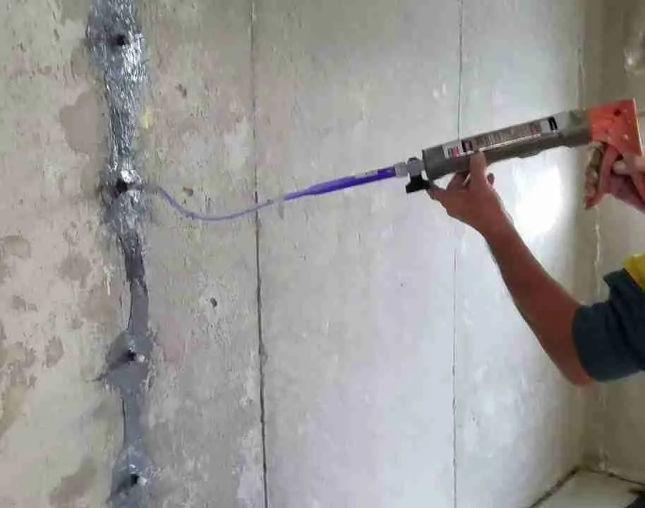 A person repairing a crack in a concrete structure with epoxy resin